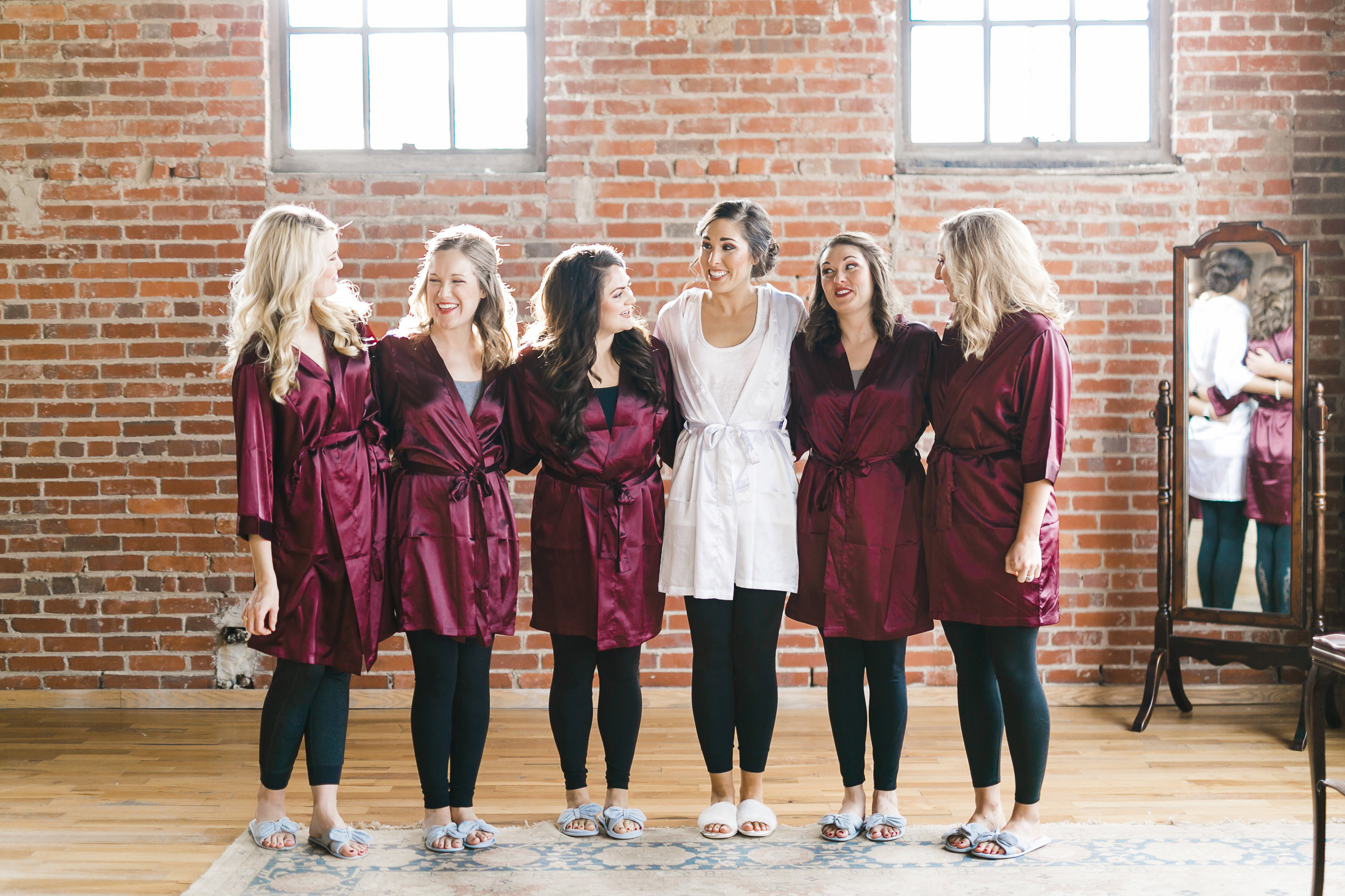 bride in white robe with five bridesmaids in maroon robes in brick room at the standard in knoxville