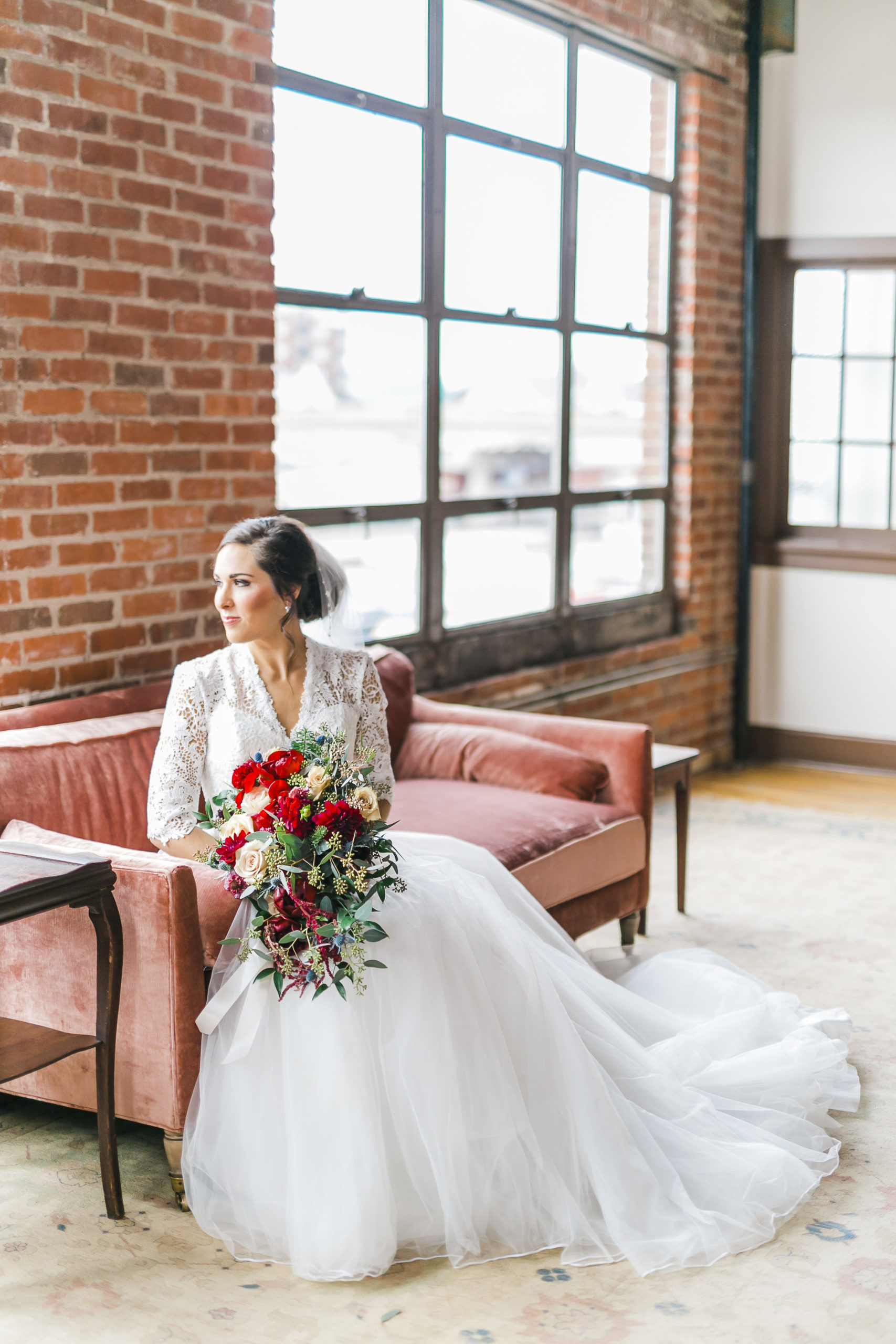 bride with ballgown and red and white flowers on pink velvet couch in brick room downtown knoxville with huge windows
