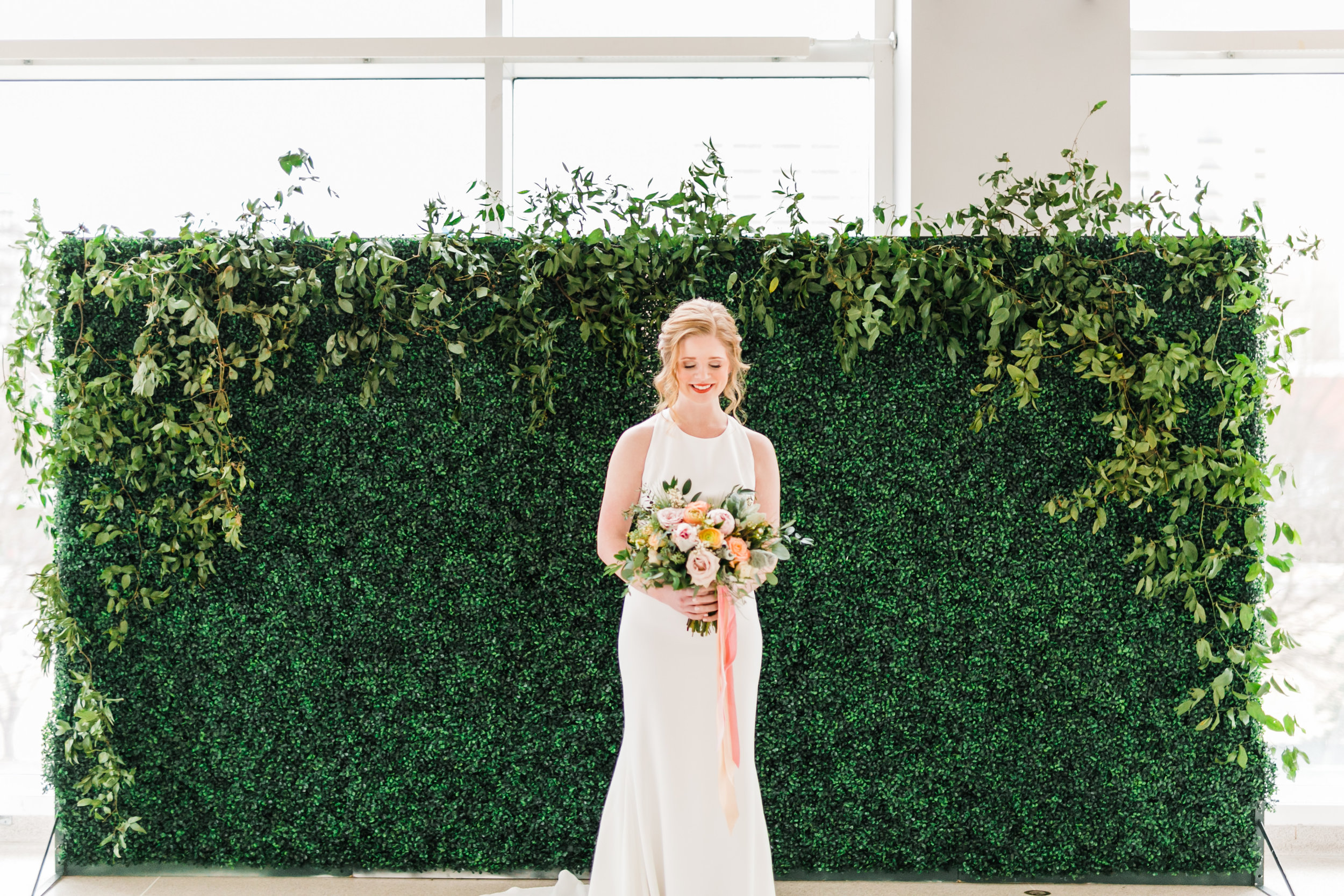 redhead bride in front of greenery wall with pink and orange bouquet