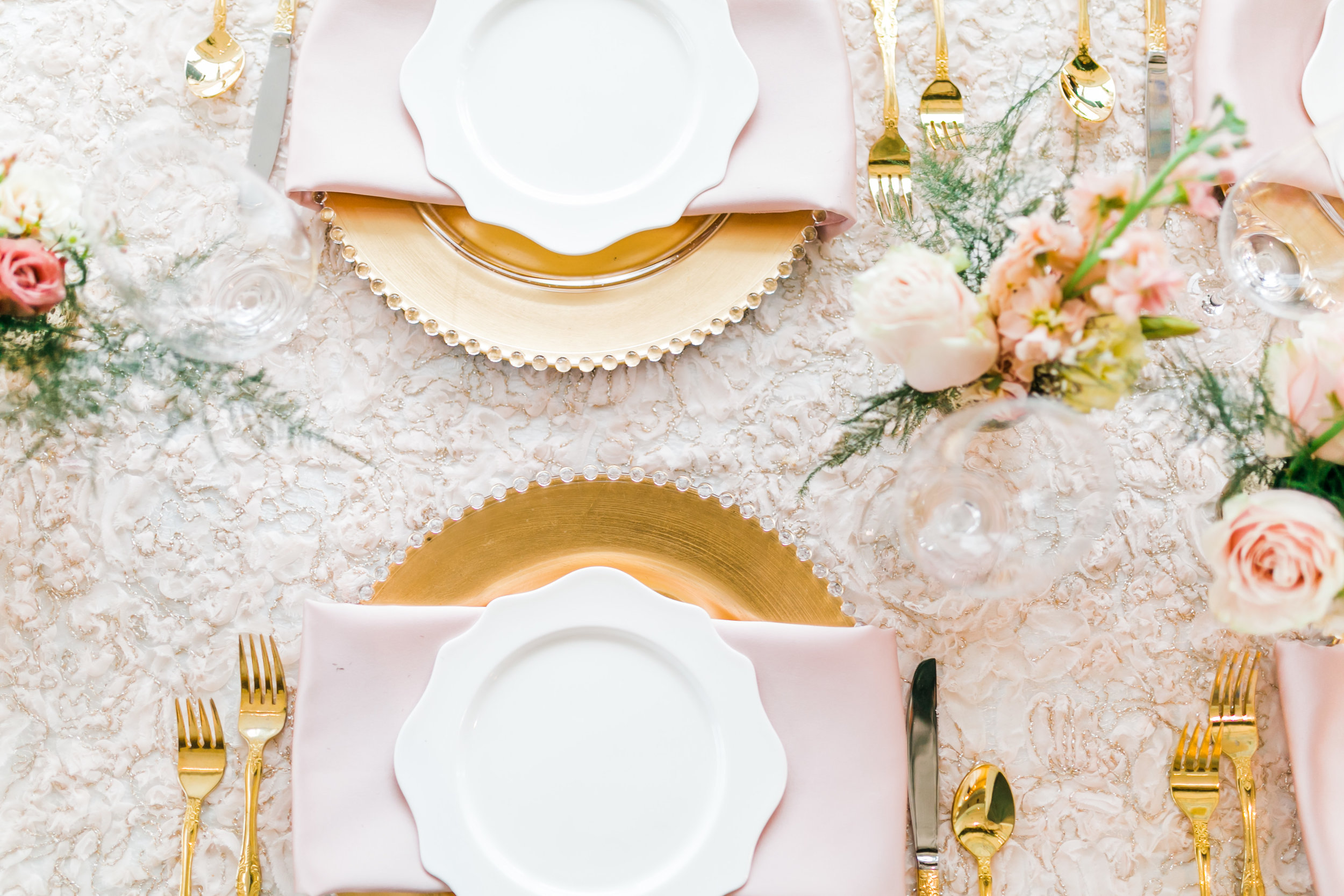 feminine table setting with gold charges and greenery and pink napkins